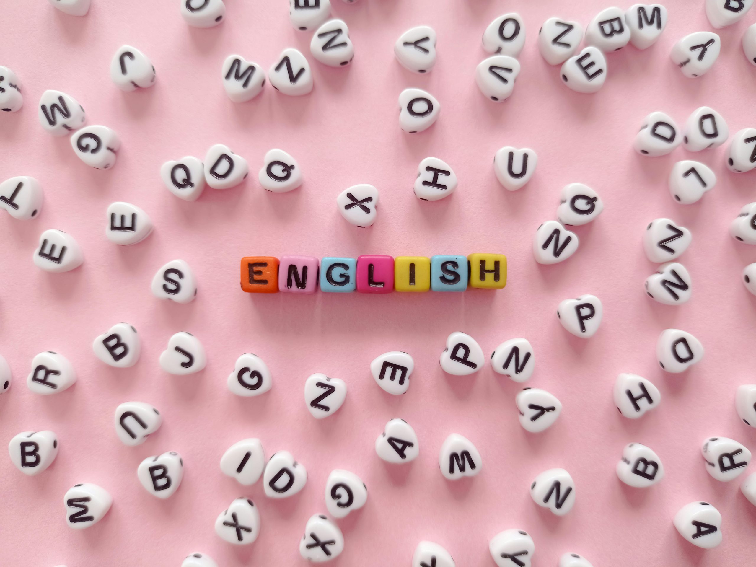 Home Scattered letter beads form the word 'English' on a pink background, symbolizing language learning.