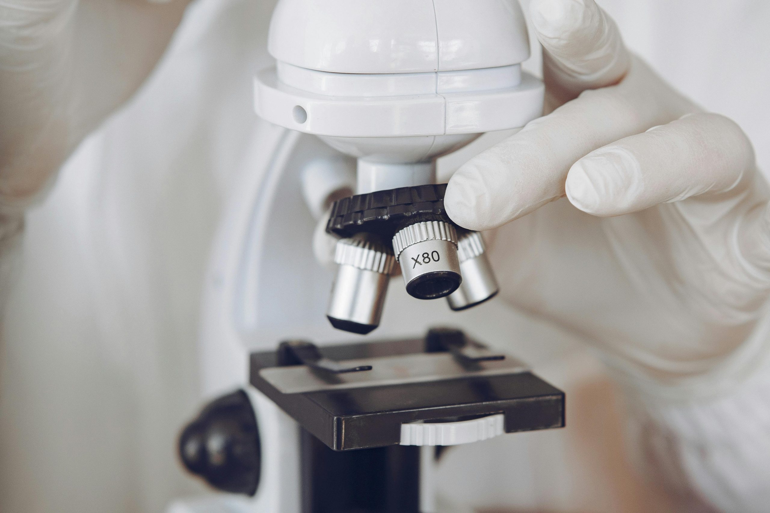 Home Gloved scientist adjusting a microscope in a laboratory setting, focusing on optics and research.