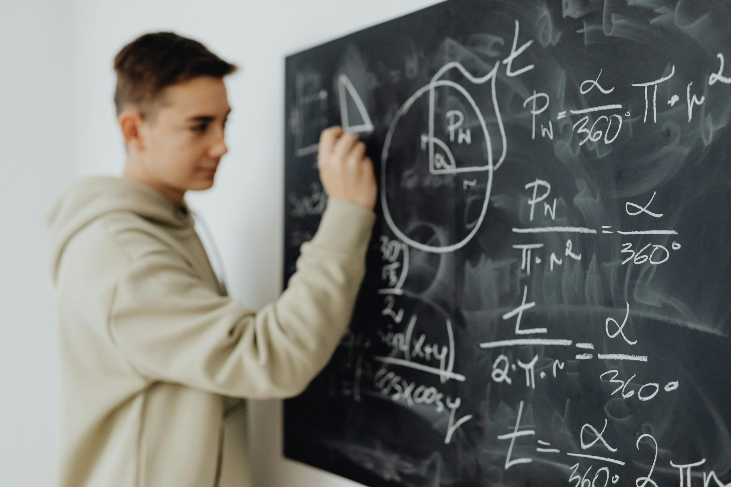 Home Focused teenager solving a math equation on a blackboard in a classroom setting.
